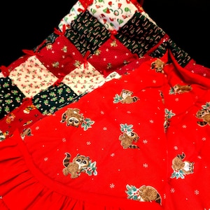 May include: A red Christmas tree skirt with a ruffled edge. The skirt is decorated with a patchwork design of red, green, and white fabric. The patchwork fabric features a variety of holiday designs, including candy canes, snowflakes, and holly.