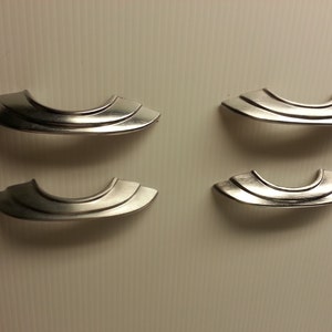 May include: Four silver cabinet door pulls with a curved, rounded design. The pulls have a smooth, polished finish.