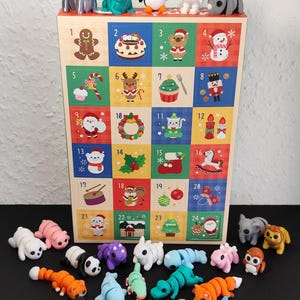 Puede incluir: Un calendario de adviento de madera con puertas numeradas, con ilustraciones coloridas con temas navideños. Figuras de animales variadas, incluyendo un pingüino, una rana y un hipopótamo, se exhiben encima y debajo del calendario. El calendario tiene 24 puertas.