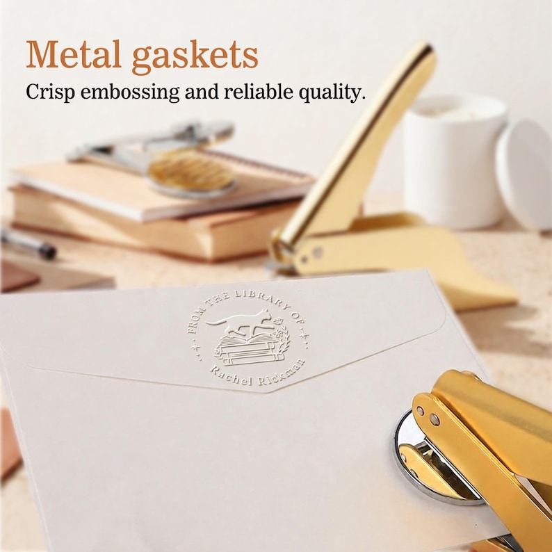 Peut inclure: Une presse &agrave; cacheter en m&eacute;tal dor&eacute; &agrave; c&ocirc;t&eacute; d'une enveloppe blanche avec un motif en relief et du texte. Le texte sur l'enveloppe se lit "FROM THE LIBRARY OF... Rachel Rickman". L'image montre &eacute;galement le texte "Metal gaskets" et "Crisp embossing and reliable quality."