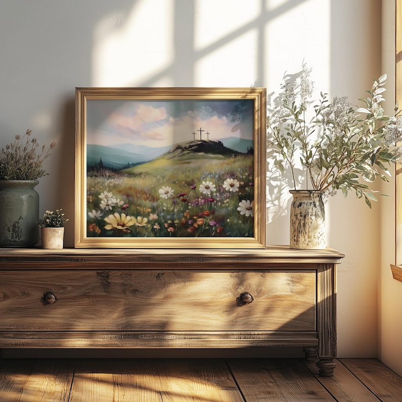 May include: A framed landscape painting depicts a grassy hill with three crosses under a cloudy sky. The foreground features a field of wildflowers in various colors. The painting is displayed on a wooden dresser, with vases of flowers and plants.
