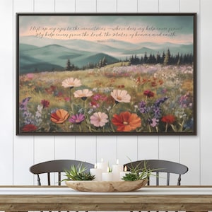 May include: A framed landscape painting depicts a field of wildflowers with mountains in the background. The artwork features a variety of colorful flowers and the text "I lift up my eyes to the mountains..." in script.