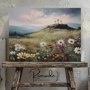 May include: A canvas print of a landscape painting featuring a grassy hill with three crosses at the top. The foreground is filled with wildflowers in shades of white, yellow, and purple. The sky is a soft blend of blue and pink. The text "Riverside Art Collection" is at the bottom.