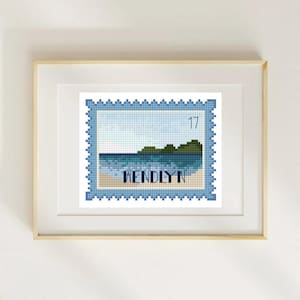 May include: A framed cross-stitch artwork featuring a beach scene within a blue postage stamp design. The artwork includes the word "WENDLYN" and the number "17". The frame is a light wood color.