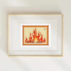 May include: A framed print featuring a postage stamp design with a pixelated image of flames in shades of orange and red. The stamp reads "AUTUMN COURT" and has a value of "60". The frame is light wood.