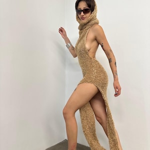 May include: A tan, fuzzy, sleeveless dress with a high slit and matching scarf-like hood. The dress is paired with black, shiny Mary Jane flats and sunglasses. The outfit is a unique, eye-catching fashion statement.