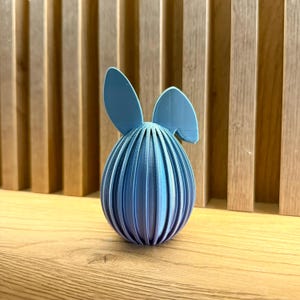 May include: A blue Easter egg with bunny ears. The egg is made of a textured material and has a light blue color.