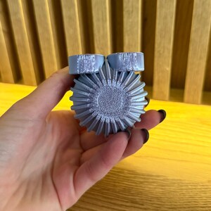 May include: A silver-colored, 3D printed, round object with a textured surface and two smaller, round, textured protrusions on top.
