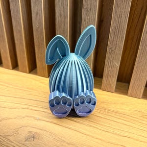 May include: A blue and purple 3D printed Easter bunny egg holder. The bunny has long ears and small feet.