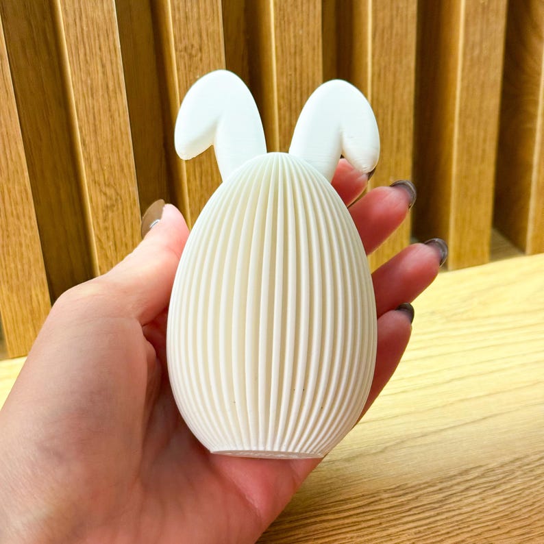 May include: White ceramic Easter egg with bunny ears. The egg has a ribbed texture and is a light white color.