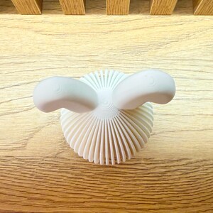 May include: White ceramic bunny sculpture with a textured, fan-shaped base and two rounded ears.