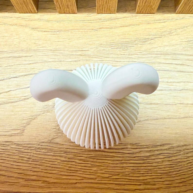 May include: White ceramic bunny sculpture with a textured, fan-shaped base and two rounded ears.