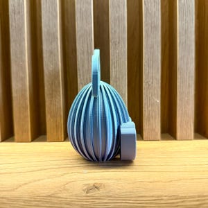 May include: A light blue ceramic egg-shaped ornament with a textured surface and a small handle on top.