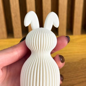 May include: White ceramic bunny figurine with a ribbed body and long, floppy ears.