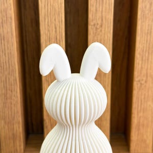 May include: White ceramic bunny figurine with a ribbed body and large ears. The bunny is standing upright.