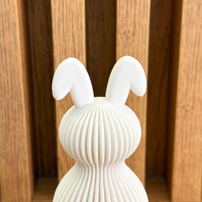 May include: White ceramic bunny figurine with a ribbed body and large ears. The bunny is standing upright.