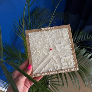 Puede incluir: Un mapa impreso en 3D de Kryvyi Rih, Ucrania, con un corazón rojo que marca una ubicación. El mapa es blanco con un marco de madera. El texto en ucraniano dice "Kryvyi Rih" y "Aquí comenzó nuestra historia 27.09.24."