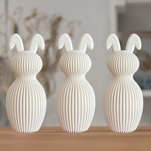 May include: Three white ceramic bunny figurines with a ribbed texture. The bunnies have long ears and a rounded body.
