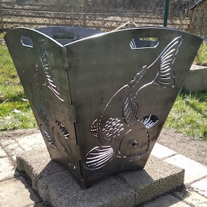 Könnte beinhalten: Ein Metall-Feuerbecken mit einem dekorativen Design aus Fisch-Ausschnitten. Das Feuerbecken steht auf einer Terrasse aus grauen Betonplatten.