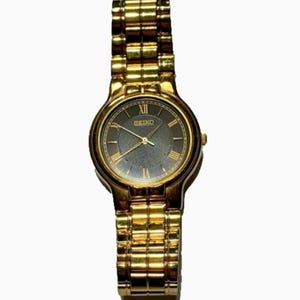 May include: Gold-toned Seiko wristwatch with a dark gray face and gold Roman numeral hour markers. The watch features a gold link band and a round watch face. The watch hands are gold. The watch is a classic design.
