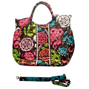 Puede incluir: Un bolso de mano acolchado marrón con estampado floral en tonos rosa, verde, azul y blanco. El bolso tiene un asa superior y una correa de hombro desmontable.