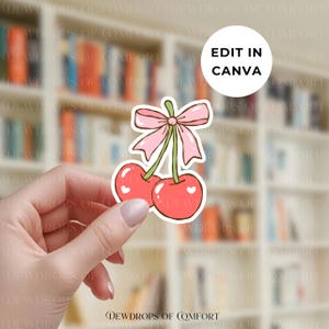 May include: A sticker featuring two red cherries with white heart details, connected by green stems and a pink bow. The sticker has a white border and the text "EDIT IN CANVA" in a white circle.