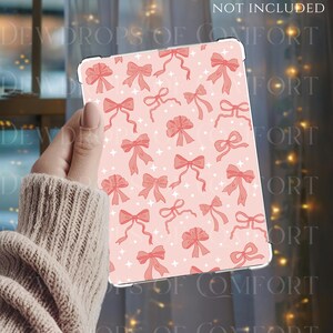 May include: A pink tablet case featuring a pattern of red bows and white star shapes. The text "EXAMPLE IMAGE NOT INCLUDED" is visible. The case is held in a hand, with the brand name "DEWDROPS OF COMFORT" at the bottom.