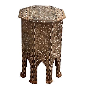 Könnte beinhalten: Ein achteckiger Beistelltisch in Dunkelbraun, verziert mit aufwendigen eingelegten floralen und geometrischen Mustern. Die Tischoberfläche und -seiten zeigen ein sich wiederholendes Muster aus weißen und dunkelbraunen Akzenten. Er hat ein markantes offenes Bein.