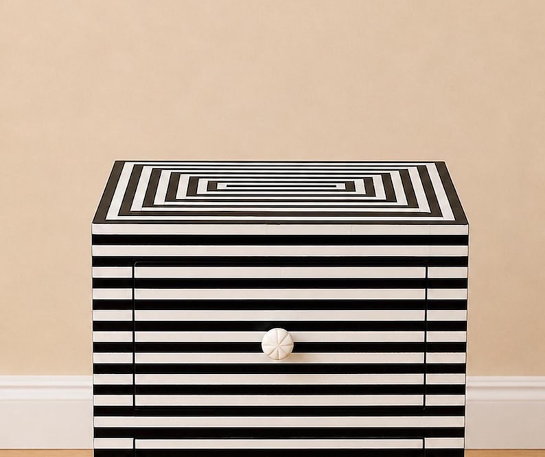 May include: A black and white striped nightstand with a geometric design on the top. The drawer features a white knob. The nightstand is a modern piece of furniture with a bold, graphic pattern.
