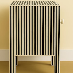 May include: A black and cream striped cabinet with a single white knob. The cabinet has a rectangular shape with four legs and a flat top. The vertical stripes create a bold, graphic pattern. The cabinet is a piece of furniture.