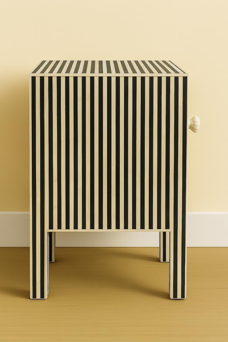 May include: A black and cream striped cabinet with a single white knob. The cabinet has a rectangular shape with four legs and a flat top. The vertical stripes create a bold, graphic pattern. The cabinet is a piece of furniture.