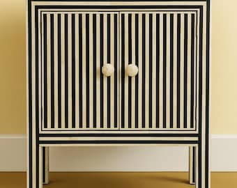 May include: A black and white striped cabinet with two doors and two round, off-white knobs. The cabinet has a rectangular shape and is supported by four legs. The design features vertical stripes and a contrasting border.