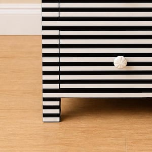 May include: A black and white striped dresser with a single drawer. The drawer has a white, starburst-shaped knob. The dresser is made of wood and has a modern design. The legs of the dresser are also striped.
