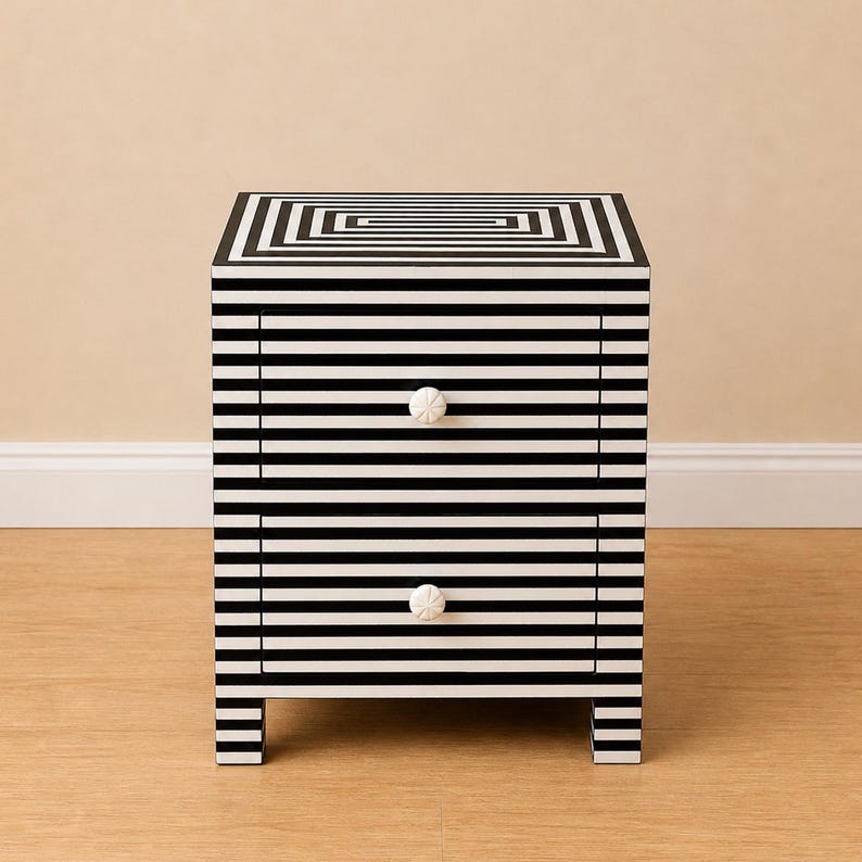 May include: A two-drawer nightstand with a black and white striped design. The top features a concentric square pattern, and the drawers have white, floral-shaped knobs. The nightstand is a modern piece of furniture.