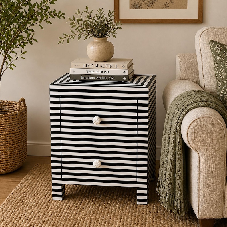 May include: A black and white striped nightstand with two drawers and white floral knobs. The nightstand has a rectangular shape and is made of wood. On top are books and a vase with greenery.