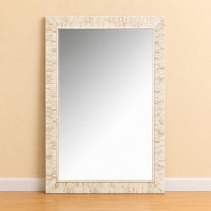 Puede incluir: Un espejo de pared rectangular con un marco ancho construido con numerosas baldosas rectangulares pequeñas de color beige claro y crema, dispuestas en un patrón apilado similar a ladrillos. La superficie reflectante es lisa.