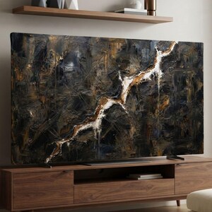 Puede incluir: Un televisor de pantalla plana grande que muestra una pintura abstracta con tonos oscuros negros, marrones y dorados, con una prominente línea diagonal dentada blanca y dorada, sobre un mueble de madera con estante.