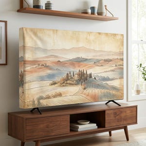 Op de afbeelding: Een rechthoekige tv-schermhoes met een aquarel-landschapsillustratie van glooiende heuvels, cipressen en een villa in gedempte aardetinten zoals beige, bruin en zachtblauw, ontworpen om over een flatscreen-televisie te passen.