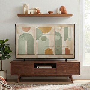 May include: A television screen displaying a triptych of abstract art featuring sage green, mustard yellow, and cream geometric shapes, including arches and circles, set on a dark wood media console with a matching shelf above holding ceramic decor.