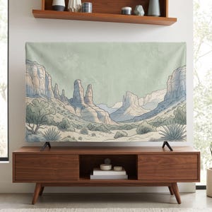 Puede incluir: Un tapiz de pared rectangular que presenta una ilustración de un paisaje desértico con imponentes formaciones rocosas, vegetación escasa y plantas de agave en una paleta de colores apagados de verde salvia, azul suave y tonos crema.