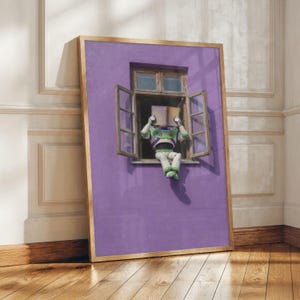 May include: A framed print featuring a whimsical scene of a Buzz Lightyear figure reading a book while seated in a window. The window is set in a purple wall, and the frame has a natural wood finish. The artwork is displayed on a wooden floor.