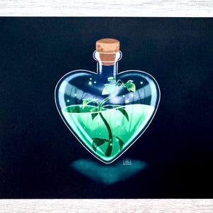 May include: A heart-shaped glass bottle with a cork stopper filled with a green liquid and a small green plant inside.