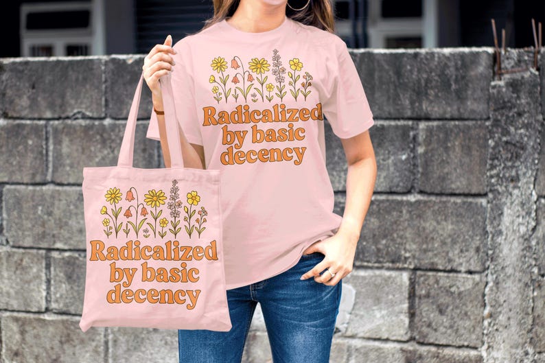 May include: A light pink t-shirt and tote bag with the text "Radicalized by basic decency" in orange. Both items feature a floral design. The person is wearing blue jeans.