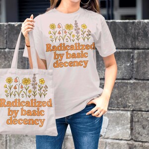May include: White t-shirt and tote bag with a floral design and the text "Radicalized by basic decency" in orange. The tote bag is held by a person wearing blue jeans.