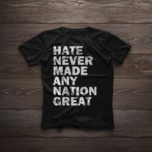 Może przedstawiać: Czarny T-shirt z białym tekstem, który brzmi "Nienawiść nigdy nie uczyniła żadnego narodu wielkim".