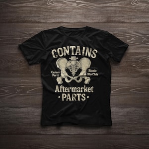 Puede incluir: Camiseta negra con un gráfico de una pelvis humana y las palabras "CONTAINS Aftermarket PARTS". El diseño incluye las frases "Custom Parts" y "Bionic Hip Club".