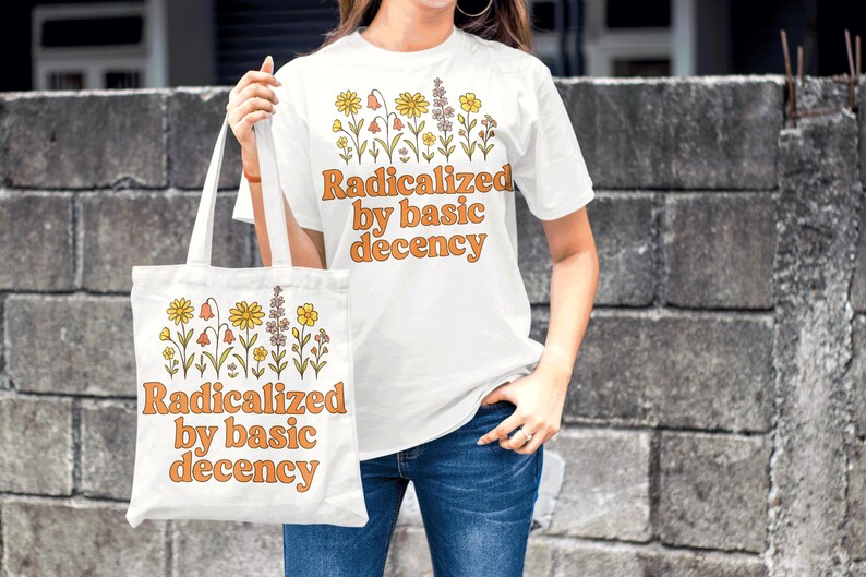 May include: White t-shirt and tote bag with the text "Radicalized by basic decency" in orange lettering. Both items feature a floral design in yellow, orange, and purple. The person is wearing blue jeans.