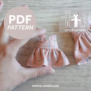 Puede incluir: Un vestido melocotón en miniatura con un estampado floral se sostiene en una mano. El vestido tiene una falda con volantes y un corpiño ajustado. La imagen incluye el texto "PDF PATTERN" y "DIGITAL DOWNLOAD". El logotipo de "LITTLE CRITTERS" también es visible.