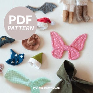 Può includere: Assortimento di elementi di costume in tessuto, tra cui un cappello da pirata, un cappello da cowboy, un cappello da elfo e ali di farfalla rosa a pois. L'immagine presenta anche un cappello di Babbo Natale, un mantello con cappuccio e una coda di sirena. Il testo "PDF PATTERN" è visibile.