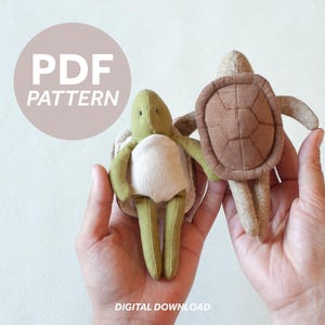Peut inclure: Deux peluches tortues faites à la main, vertes, marron et beiges. Une tortue est tenue dans chaque main. Le texte "PDF PATTERN" est dans un cercle rose clair, et "DIGITAL DOWNLOAD" est en dessous.